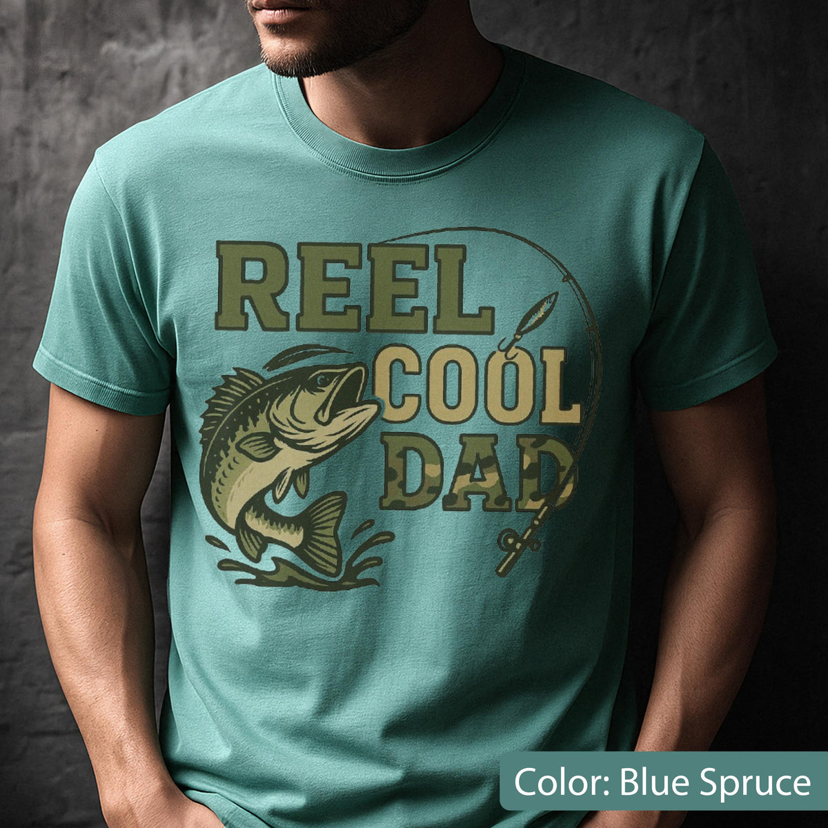 May include: Blue spruce t-shirt with the text "REEL COOL DAD" in green and camouflage lettering. A graphic of a leaping fish and fishing rod are also featured on the shirt.