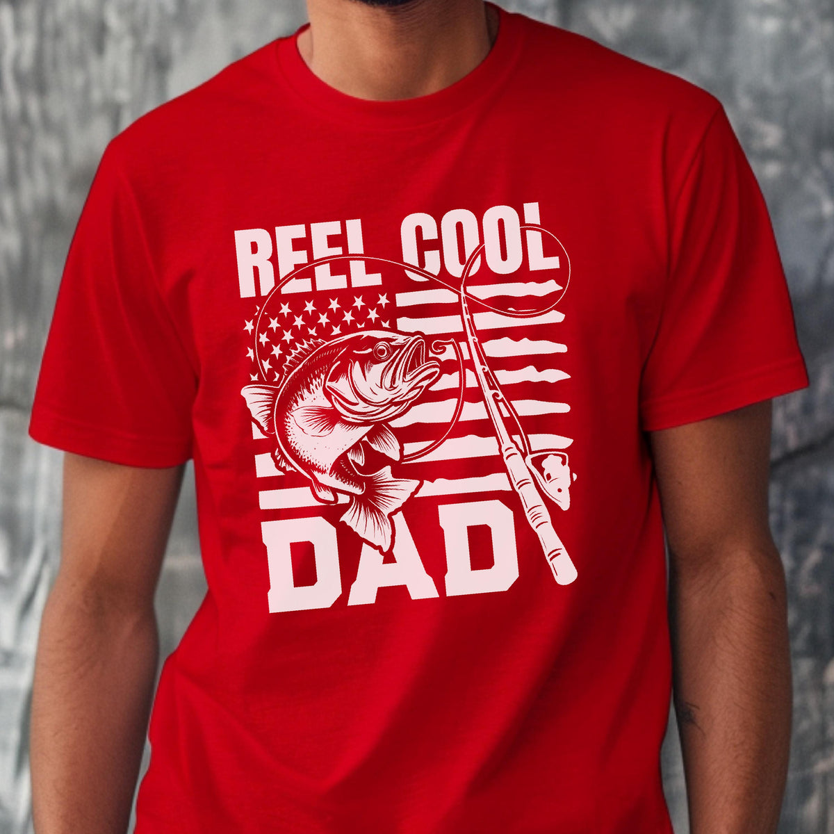 May include: Red t-shirt with a white graphic featuring a fish, fishing rod, and the words "REEL COOL DAD." The design incorporates an American flag motif, with stars and stripes. The shirt is a solid red color.