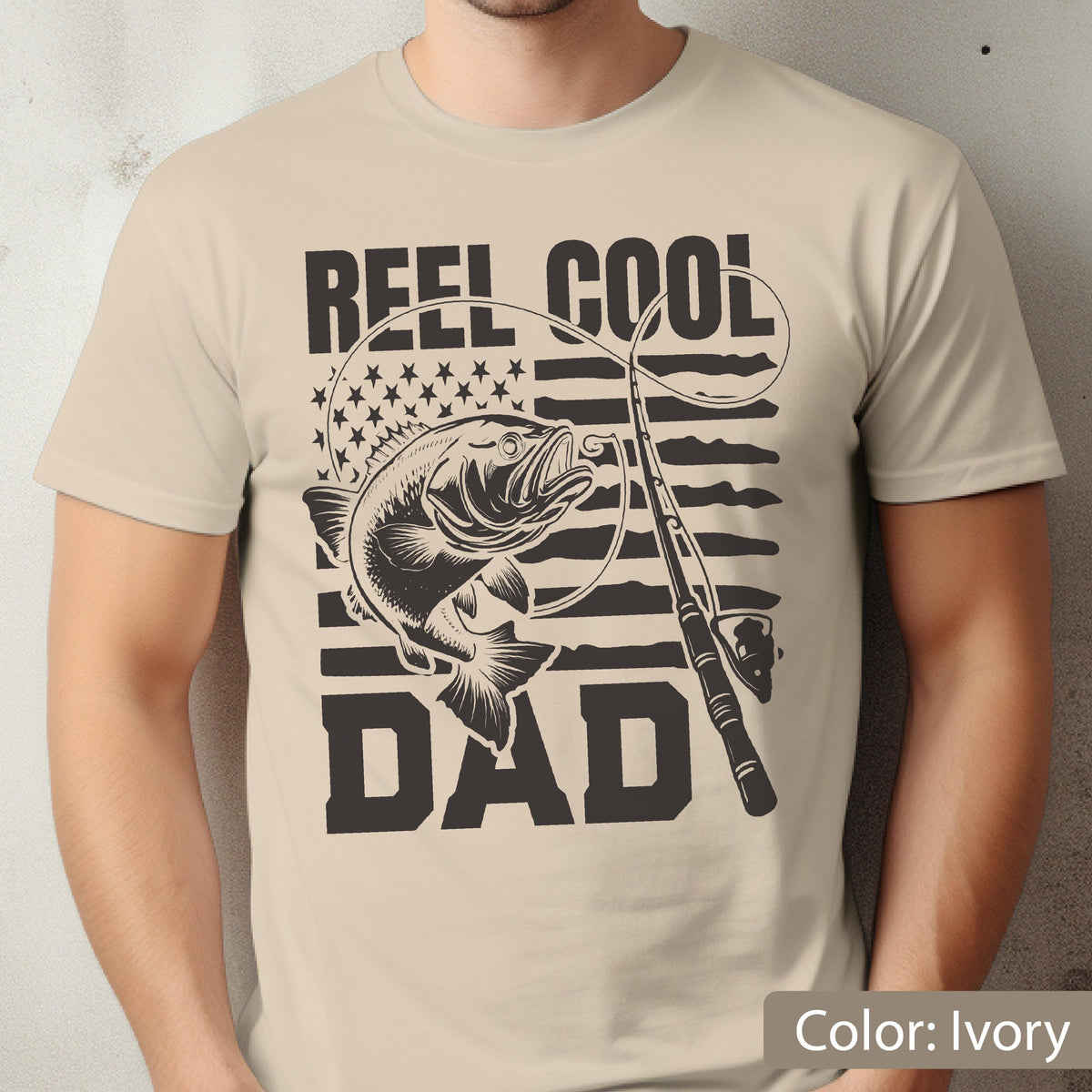 May include: Ivory-colored t-shirt featuring a graphic of a fish, fishing rod, and the text "REEL COOL DAD." The design incorporates an American flag motif. The shirt is a casual wear item.