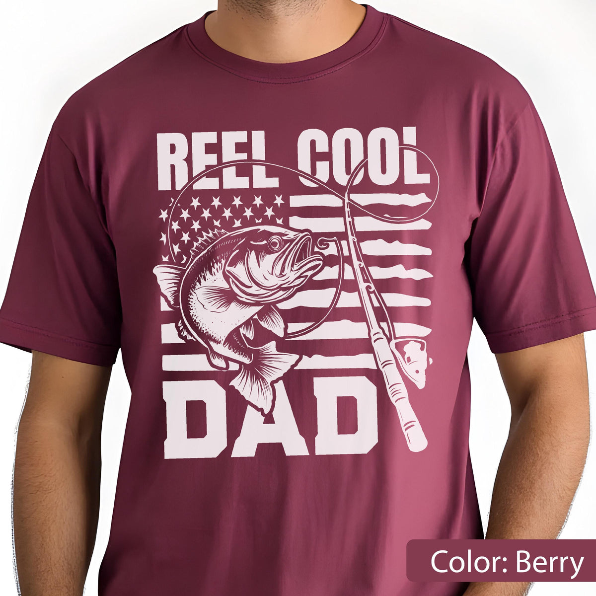 May include: Berry-colored t-shirt with a white graphic featuring a fish, fishing rod, and the words "REEL COOL DAD." The design incorporates elements of the American flag. A casual tee for fishing enthusiasts.