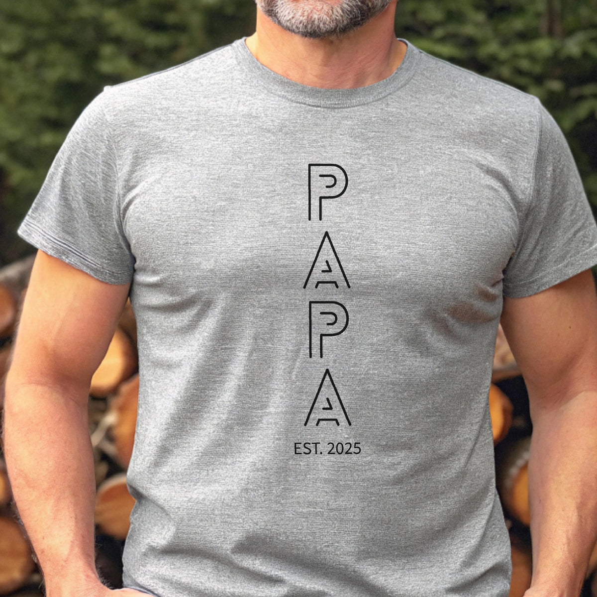 May include: A gray t-shirt with the word "PAPA" in a vertical, modern font. Below the word "PAPA" is the text "EST. 2025" in a similar font. The shirt is short-sleeved and appears to be made of a soft material.