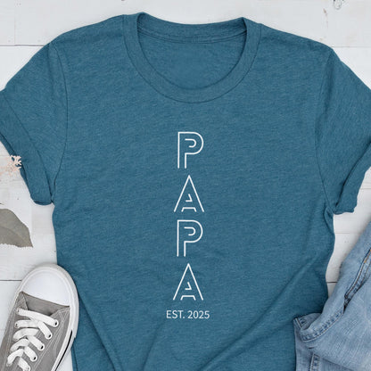 May include: Teal t-shirt with the word "PAPA" in white, vertical, outlined letters. Below the word "PAPA" is the text "EST. 2025". The shirt is made of a soft material and is suitable for casual wear.