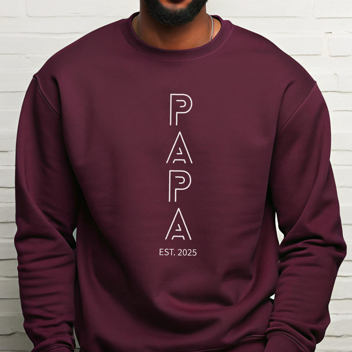 May include: A maroon sweatshirt with the word "PAPA" in white, stacked vertically. Below the word "PAPA" is the text "EST. 2025". The sweatshirt is a solid color and has a crew neck.
