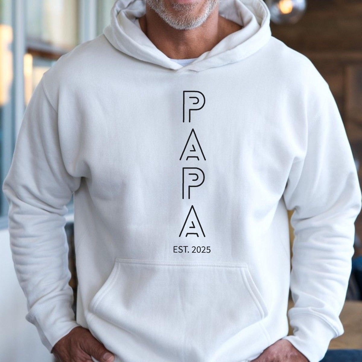 May include: Cream-colored hoodie with a front pocket and a drawstring hood. The word "PAPA" is printed vertically in black, with "EST. 2025" below it. The hoodie is made of a soft, comfortable material.