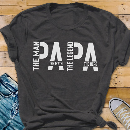 May include: Dark gray t-shirt with the word "PAPA" in large white letters. The words "The Man," "The Myth," "The Legend," and "The Hero" are also printed on the shirt in white.