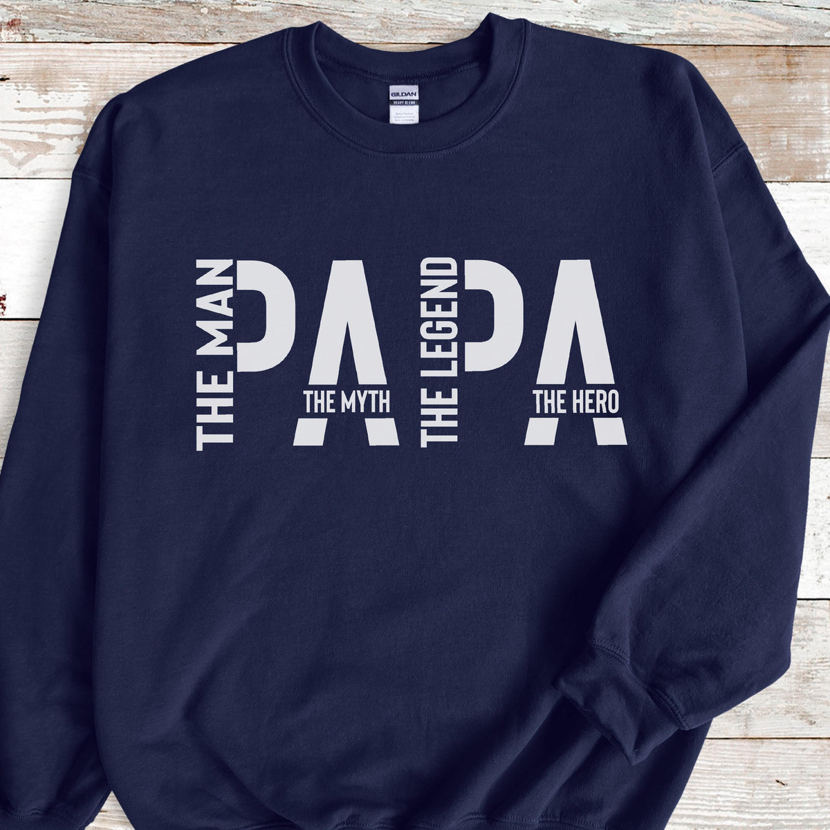 May include: Navy blue sweatshirt with the word "PAPA" in large white letters. The text "THE MAN", "THE MYTH", "THE LEGEND", and "THE HERO" are also printed in white on the sweatshirt. The sweatshirt has a crew neck and long sleeves.