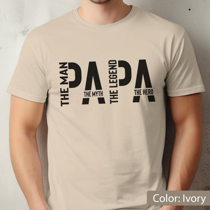May include: Ivory-colored t-shirt with the word "PAPA" in large black letters. The words "THE MAN, THE MYTH, THE LEGEND, THE HERO" are arranged around the word "PAPA". The shirt is a crew neck style.