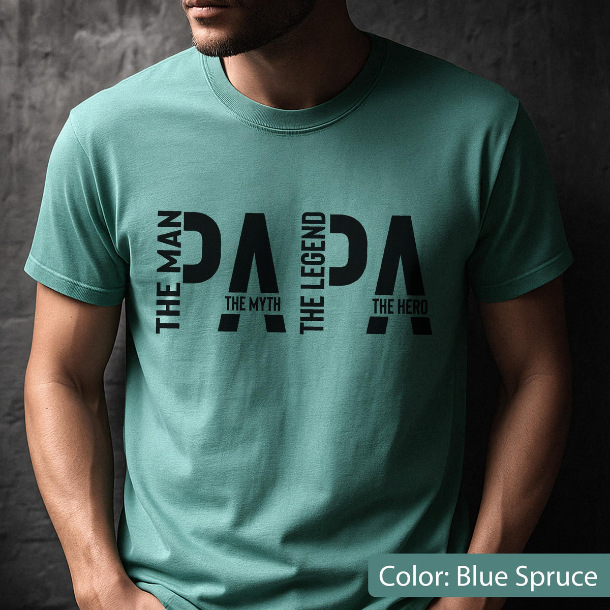 May include: Blue spruce t-shirt with the word "PAPA" in large black letters. Above "PAPA" is "THE MAN", "THE LEGEND", and "THE HERO". Below "PAPA" is "THE MYTH". The shirt is a solid color and has short sleeves.