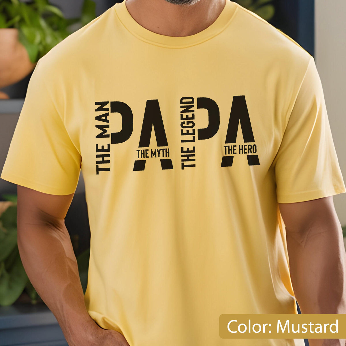 May include: Mustard yellow t-shirt with the word "PAPA" in large black letters. The words "THE MAN", "THE MYTH", "THE LEGEND", and "THE HERO" are vertically aligned on the left and right sides of the word "PAPA".