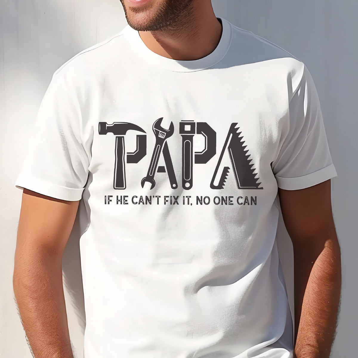 May include: White t-shirt with a black graphic design. The word "PAPA" is formed using tools like a hammer, wrench, and saw. Below the word is the text: "IF HE CAN'T FIX IT, NO ONE CAN."