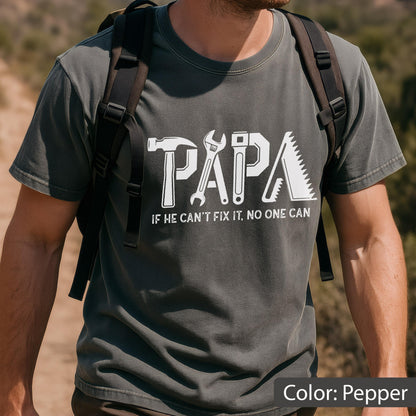 May include: Pepper-colored t-shirt with the word "PAPA" in white, featuring tool graphics. Below the word is the text "IF HE CAN'T FIX IT, NO ONE CAN". The shirt is short-sleeved.