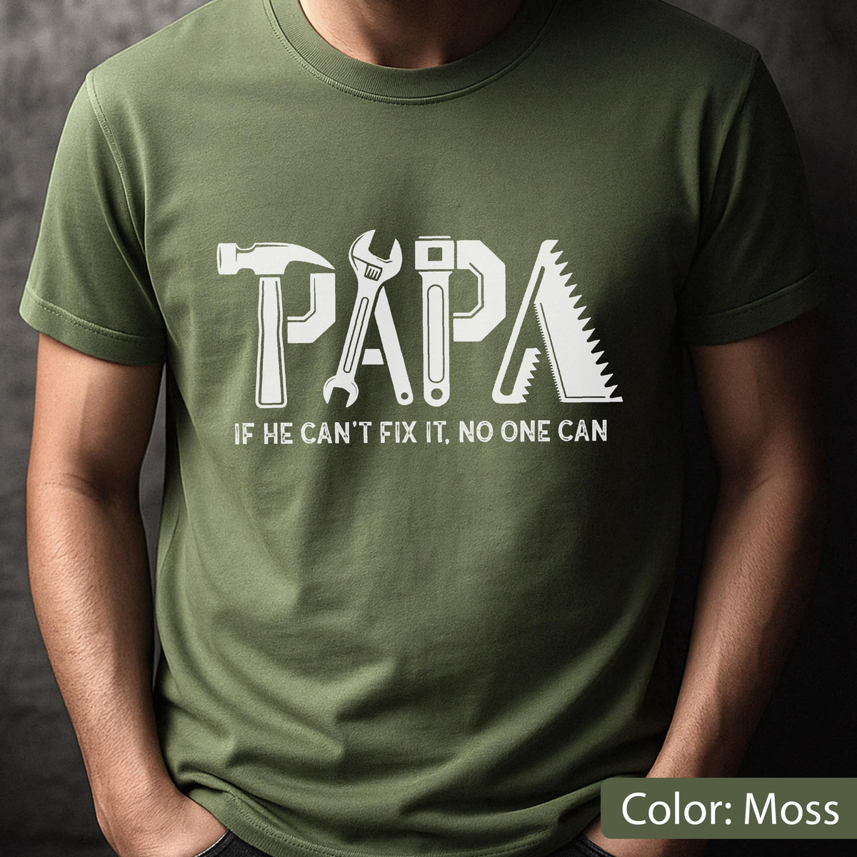 May include: Moss green t-shirt with the word "PAPA" in white, incorporating tool graphics. Below, the text reads "IF HE CAN'T FIX IT, NO ONE CAN." The shirt is a solid color and has short sleeves.