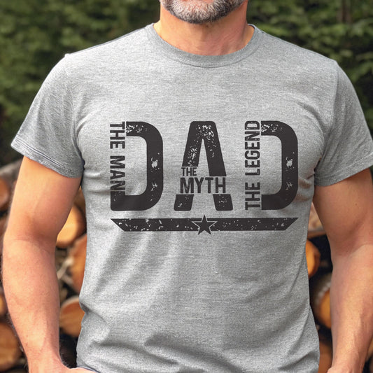 May include: A gray t-shirt with the text "DAD The Man The Myth The Legend" in distressed black lettering. A star is centered below the word "Myth". The shirt has short sleeves.