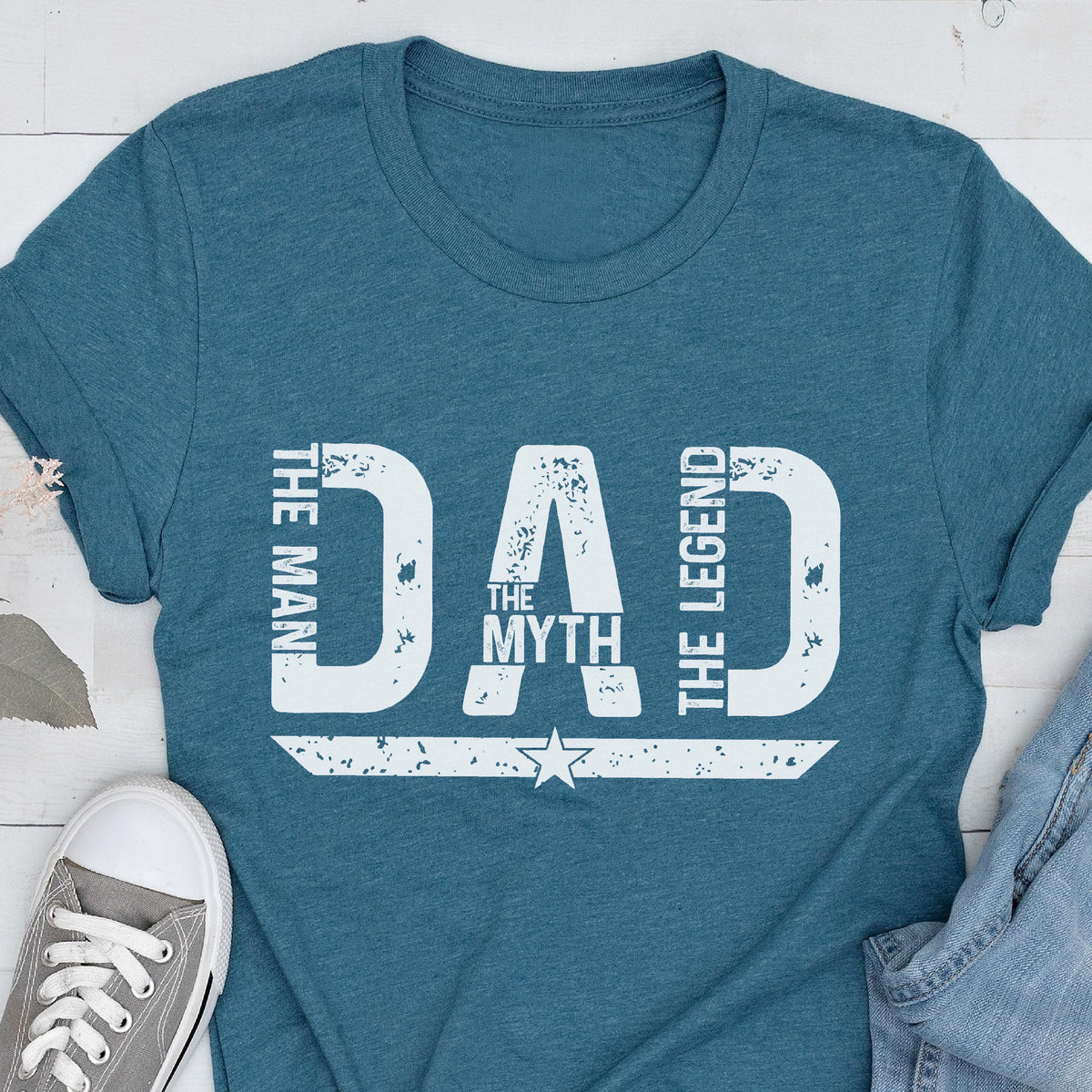May include: Teal t-shirt with the words "DAD" in large white letters. The text "THE MAN, THE MYTH, THE LEGEND" is also printed on the shirt. A star graphic is below the word "MYTH".