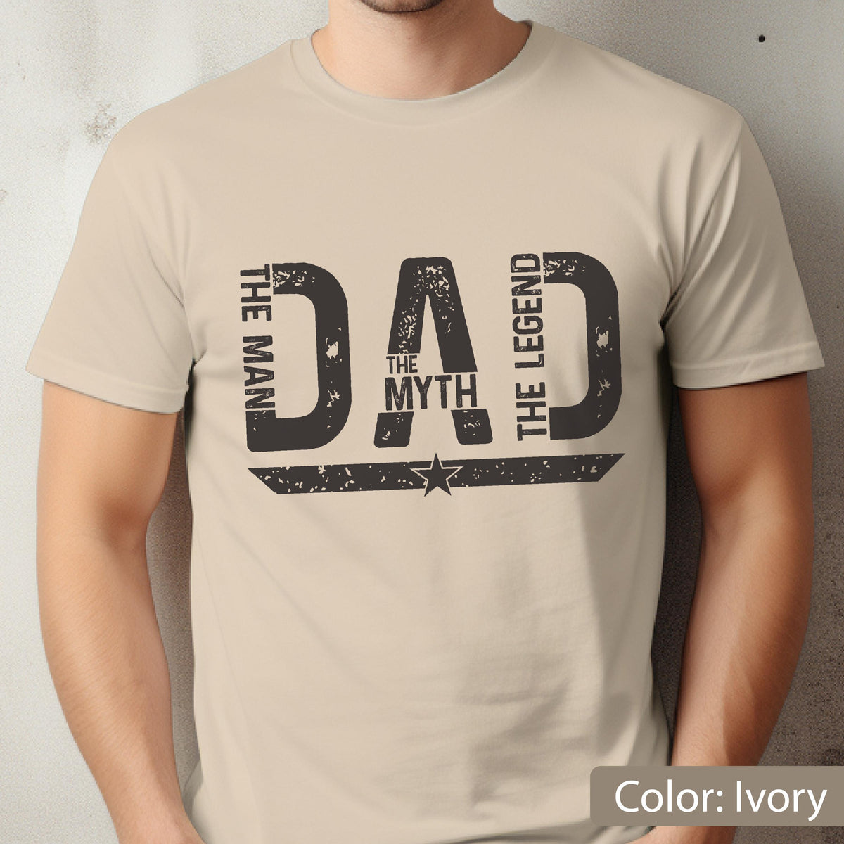 May include: Ivory-colored t-shirt with a distressed black graphic that reads "DAD" with "THE MAN", "THE MYTH", and "THE LEGEND" in a vertical arrangement. A star is centered below the word "DAD".