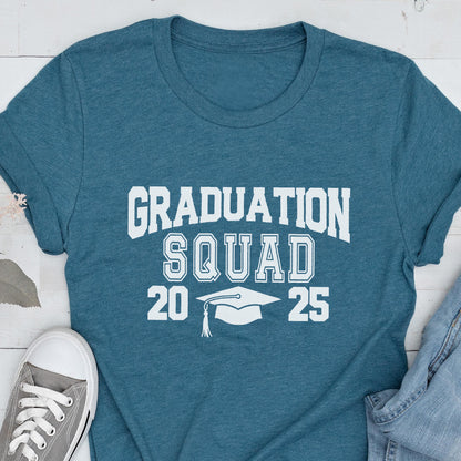 May include: Teal t-shirt with the words "GRADUATION SQUAD 2025" in white block letters. A graduation cap graphic is between the numbers. The shirt is paired with gray sneakers and blue jeans.