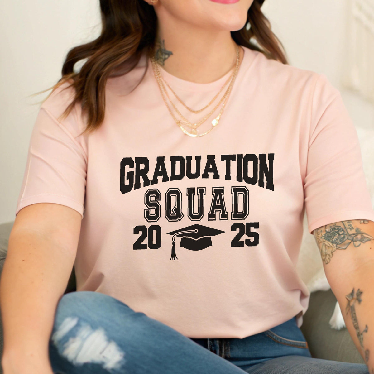 May include: A light pink t-shirt with the words "GRADUATION SQUAD 2025" in black block letters. A graduation cap graphic is between the numbers 20 and 25. The shirt is made of a soft material.