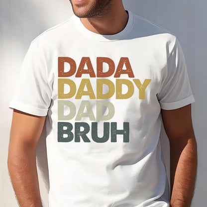 May include: White t-shirt with the words "DADA", "DADDY", "DAD", and "BRUH" in a stacked design. The text is in a retro color palette of brown, yellow, green, and gray.