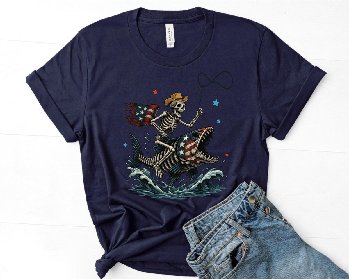 May include: Navy blue t-shirt featuring a skeleton cowboy riding a fish with an American flag design. The skeleton wears a cowboy hat and holds a lasso. The fish has an American flag design on its body. Blue waves and stars complete the design.