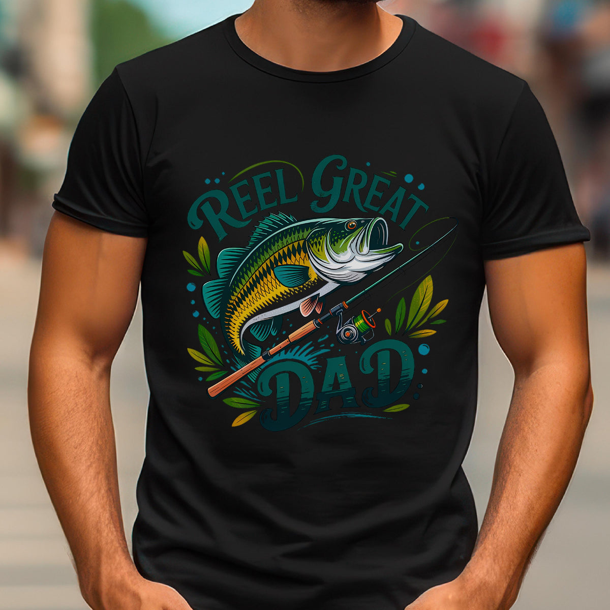 May include: Black t-shirt with a colorful graphic featuring a fish, fishing rod, and the words "Reel Great Dad" in teal and green. The design includes decorative leaves and dots, perfect for a fishing enthusiast.