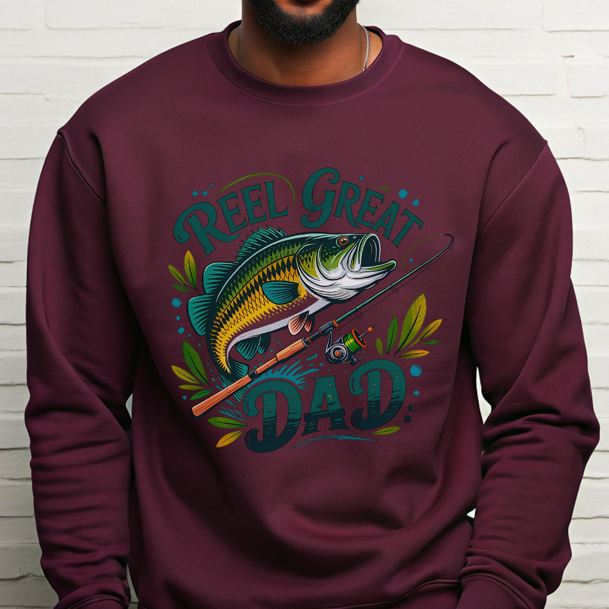 May include: Burgundy sweatshirt with a graphic of a fish, fishing rod, and the words "Reel Great Dad" in teal and green. The fish is yellow, green, and blue. The design includes decorative leaves.