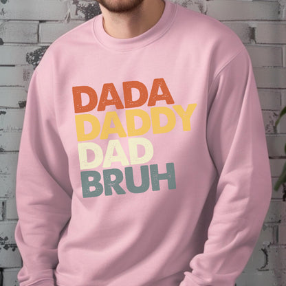 May include: A light pink sweatshirt with the words "DADA DADDY DAD BRUH" in orange, yellow, white, and teal lettering. The sweatshirt is a crew neck style.