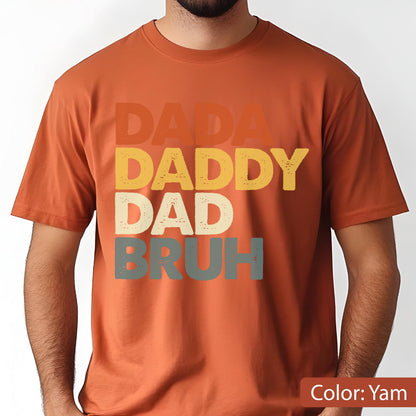 May include: A short-sleeved, yam-colored t-shirt with the words "DADA", "DADDY", "DAD", and "BRUH" stacked vertically in retro-style lettering. The text is in shades of orange, yellow, off-white, and gray.