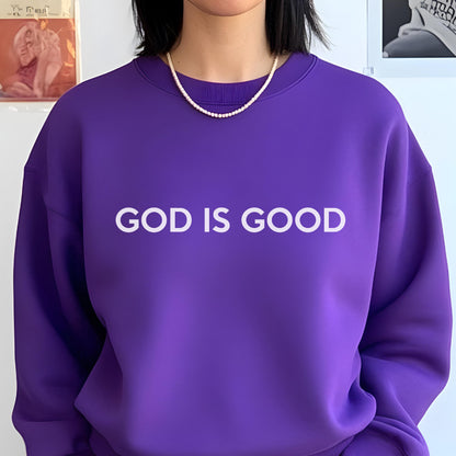 May include: A vibrant purple sweatshirt with the text "GOD IS GOOD" in white block letters. The crew neck sweatshirt is paired with a pearl necklace. The image is a close-up of the upper body.