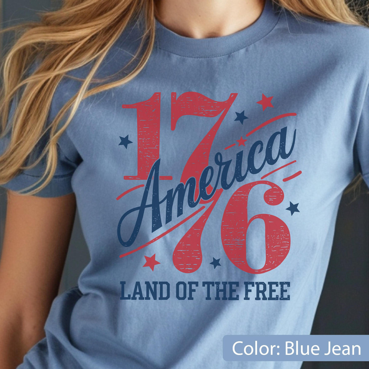 May include: A light blue t-shirt with the text "1776 America" in red and blue, along with stars and the phrase "Land of the Free." The shirt is a solid color and has short sleeves.