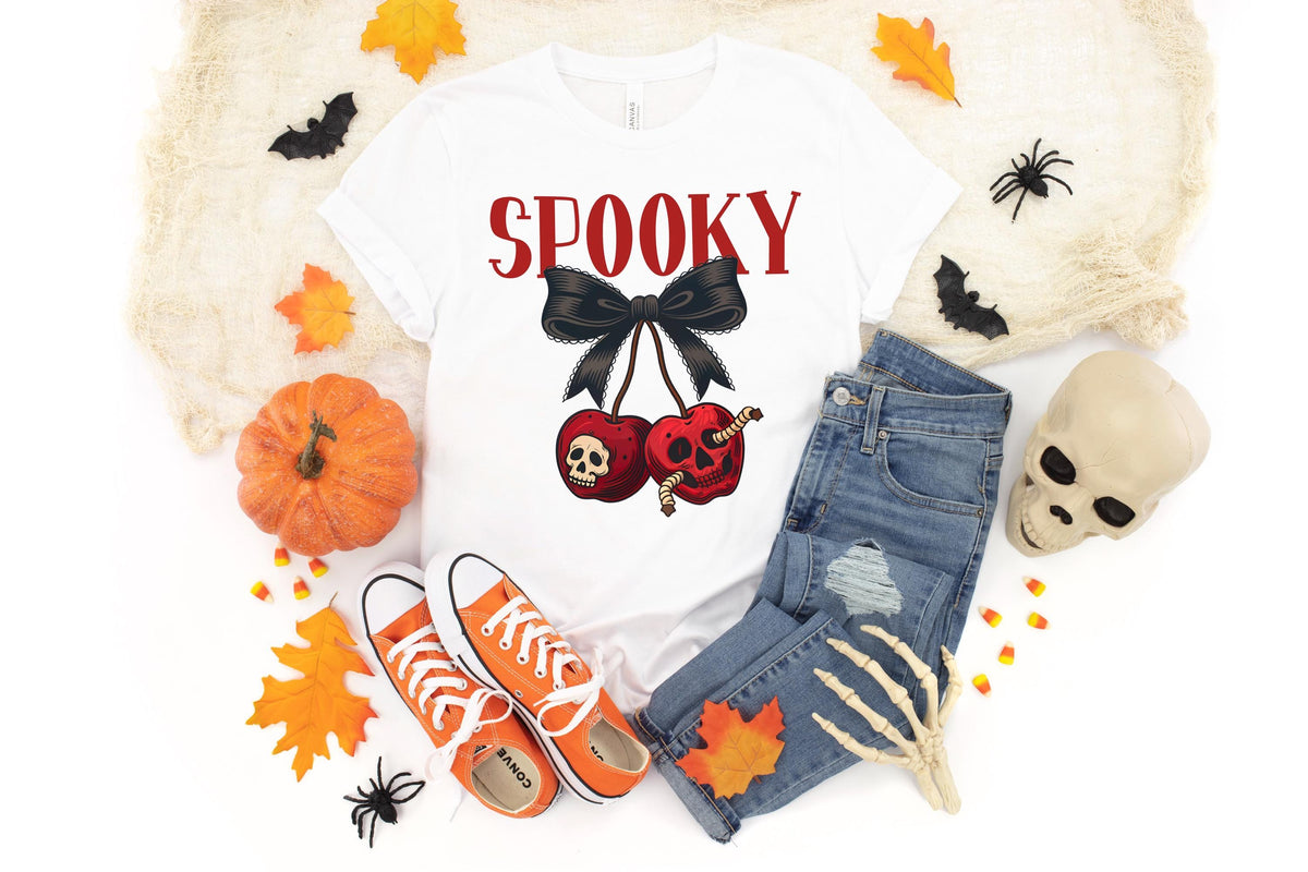 May include: White t-shirt with the word "Spooky" in red, a black bow, and two red cherries with skull and worm graphics. The shirt is paired with blue jeans, orange sneakers, and Halloween decorations.