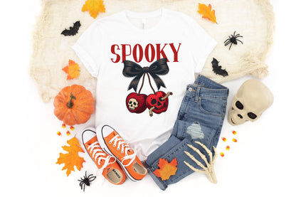 May include: White t-shirt with the word "Spooky" in red, a black bow, and two red cherries with skull and worm graphics. The shirt is paired with blue jeans, orange sneakers, and Halloween decorations.