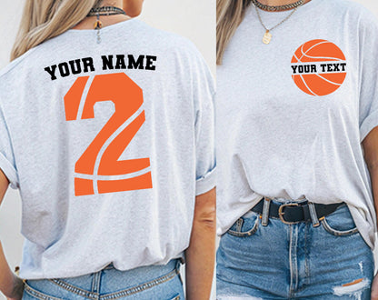 May include: A light gray t-shirt featuring a basketball-themed design. The back displays the text YOUR NAME above a large orange number 2 with basketball lines. The front features a circular basketball graphic with the text YOUR TEXT.