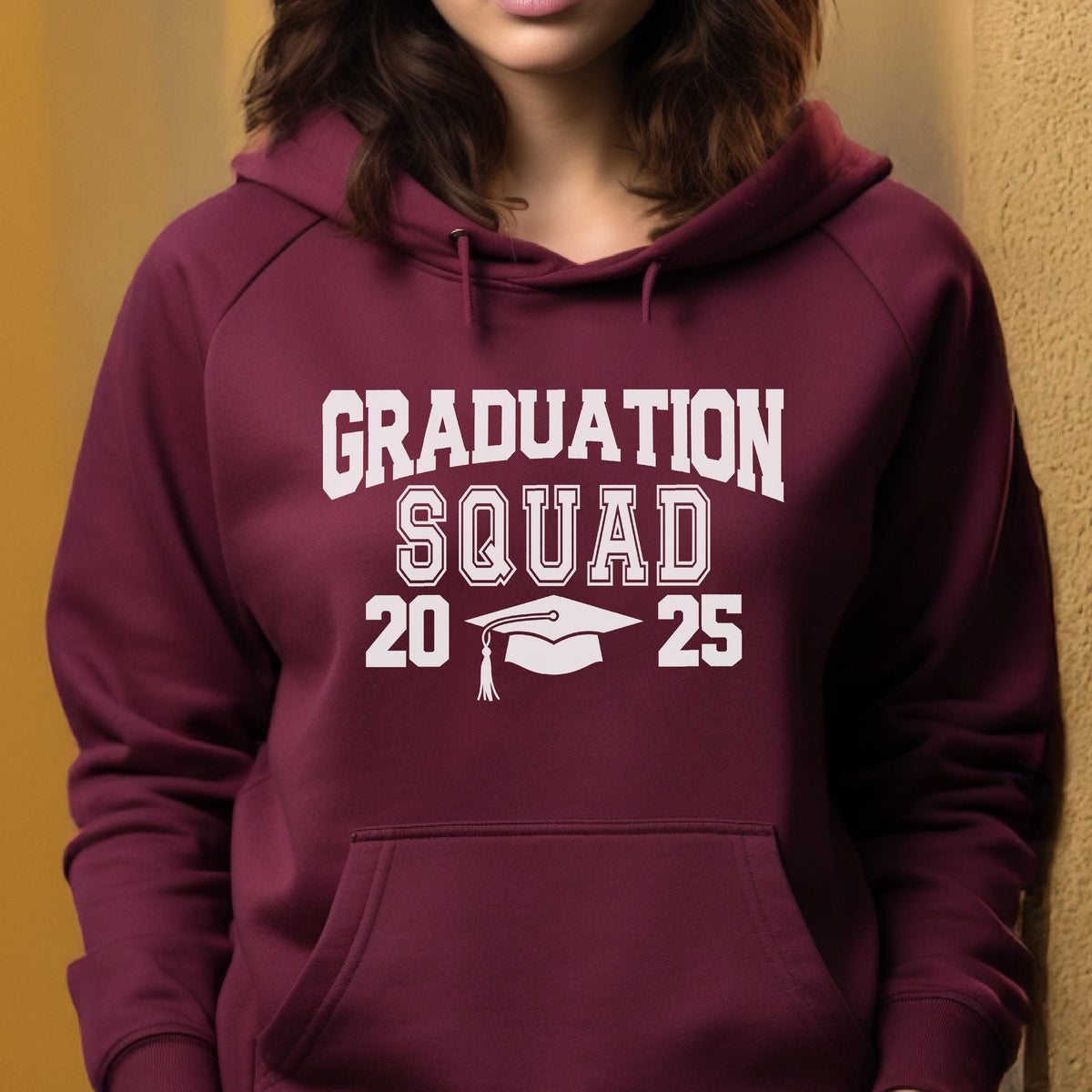 May include: A maroon hooded sweatshirt with the words "GRADUATION SQUAD" in white block letters. Below the text are the numbers "20" and "25" flanking a white graduation cap graphic. The sweatshirt has a front pocket and a drawstring hood.