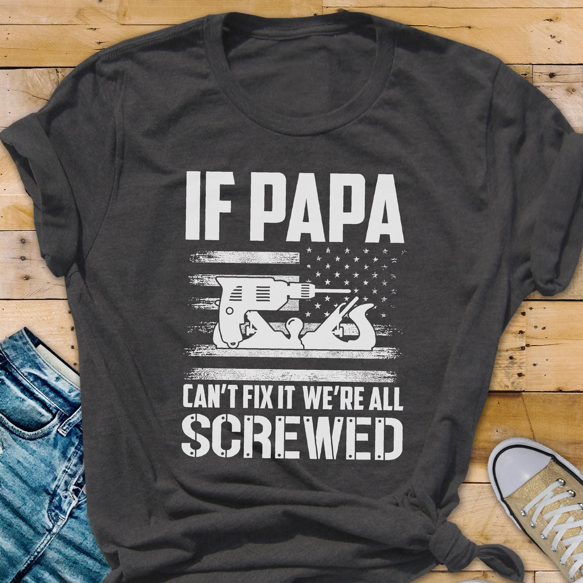 May include: Dark gray t-shirt with the text "IF PAPA CAN'T FIX IT WE'RE ALL SCREWED." The design features a drill and a hand plane in a white graphic, set against a stylized American flag.