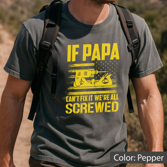 May include: Pepper-colored t-shirt with a yellow graphic design. The design features the text "IF PAPA CAN'T FIX IT WE'RE ALL SCREWED" above an illustration of a drill and a hand plane. The shirt has a crew neck and short sleeves.