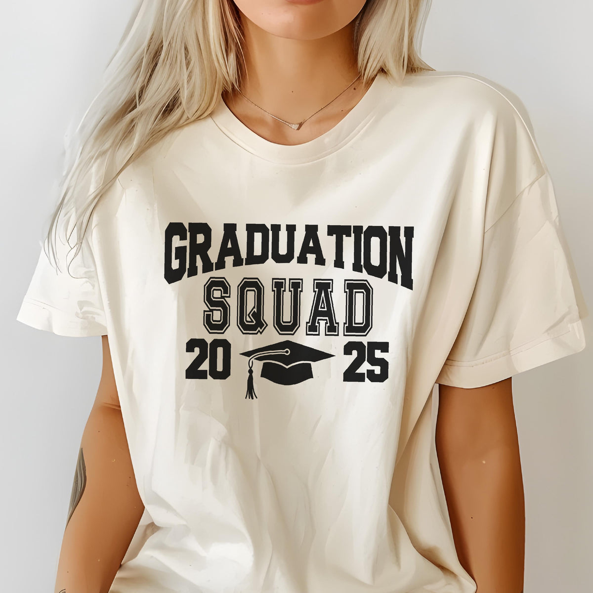 May include: Cream-colored t-shirt with the words "GRADUATION SQUAD" in bold black letters. Below, the numbers "20" and "25" flank a black graduation cap graphic. The shirt is a casual style, suitable for a graduation celebration.