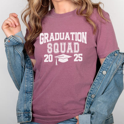 May include: A mauve-colored t-shirt with the words "GRADUATION SQUAD 20 25" printed in white. The design includes a graduation cap. The shirt is paired with a denim jacket.