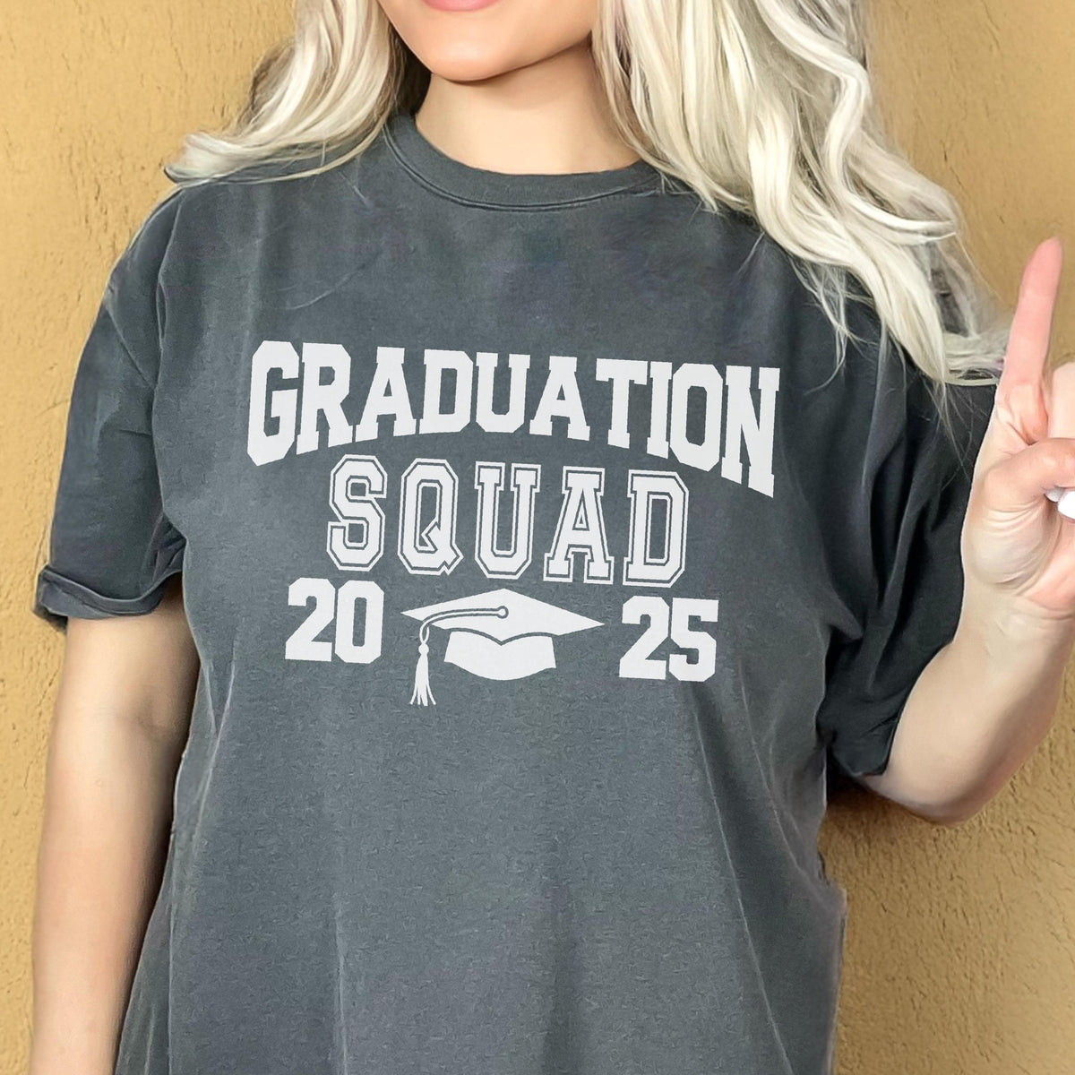 May include: Dark gray t-shirt with the words "GRADUATION SQUAD 2025" in white block letters and a graduation cap graphic. The shirt is a casual style, suitable for graduation celebrations.