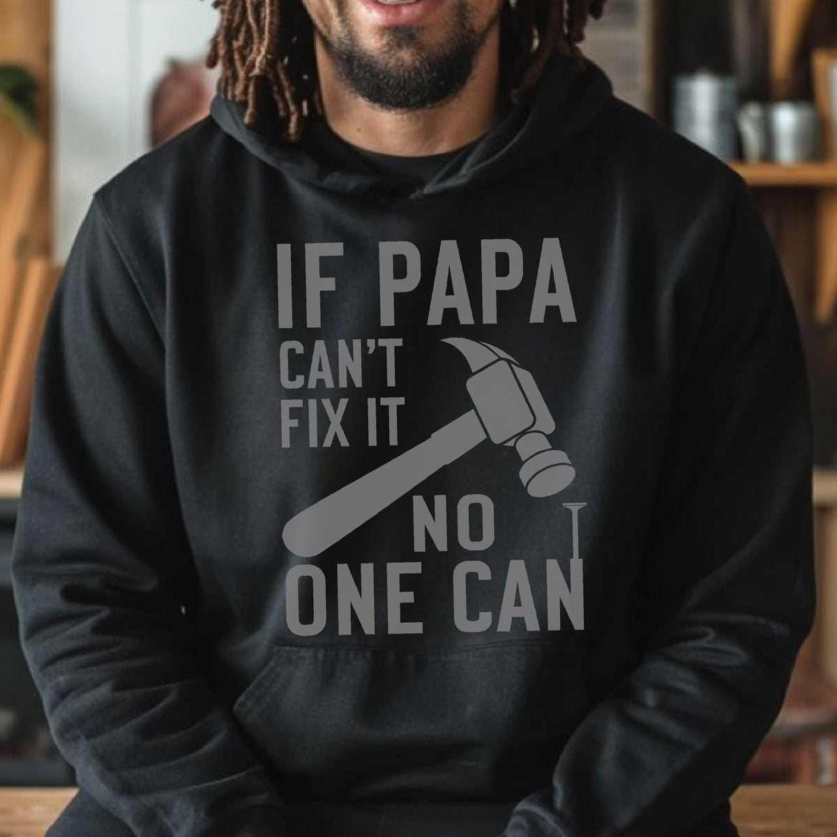 May include: Black hoodie with the text "IF PAPA CAN'T FIX IT NO ONE CAN" in gray. A gray hammer and nail graphic are also featured on the front. The hoodie has a front pocket and a drawstring hood.