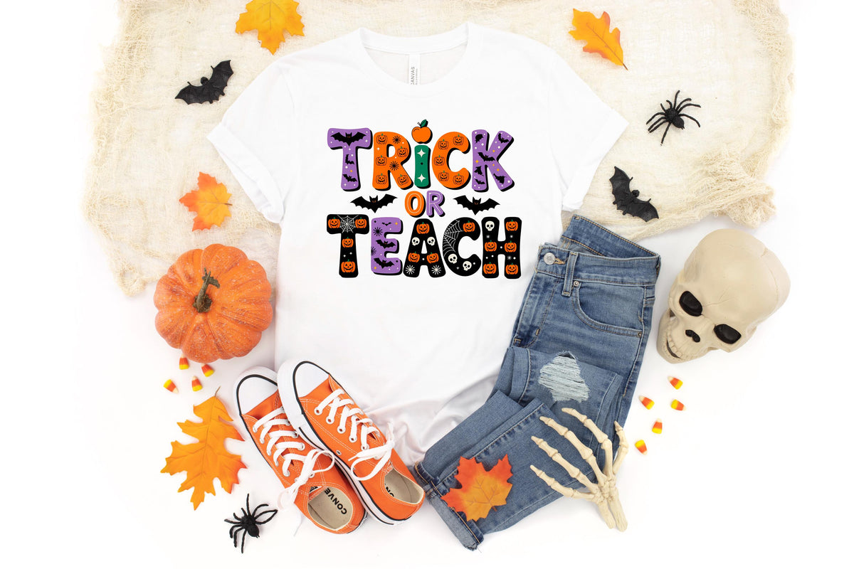 May include: White t-shirt with the words "Trick or Teach" in orange, purple, and black, with Halloween-themed graphics. The shirt is paired with blue jeans, orange sneakers, and Halloween decorations like pumpkins and spiders.