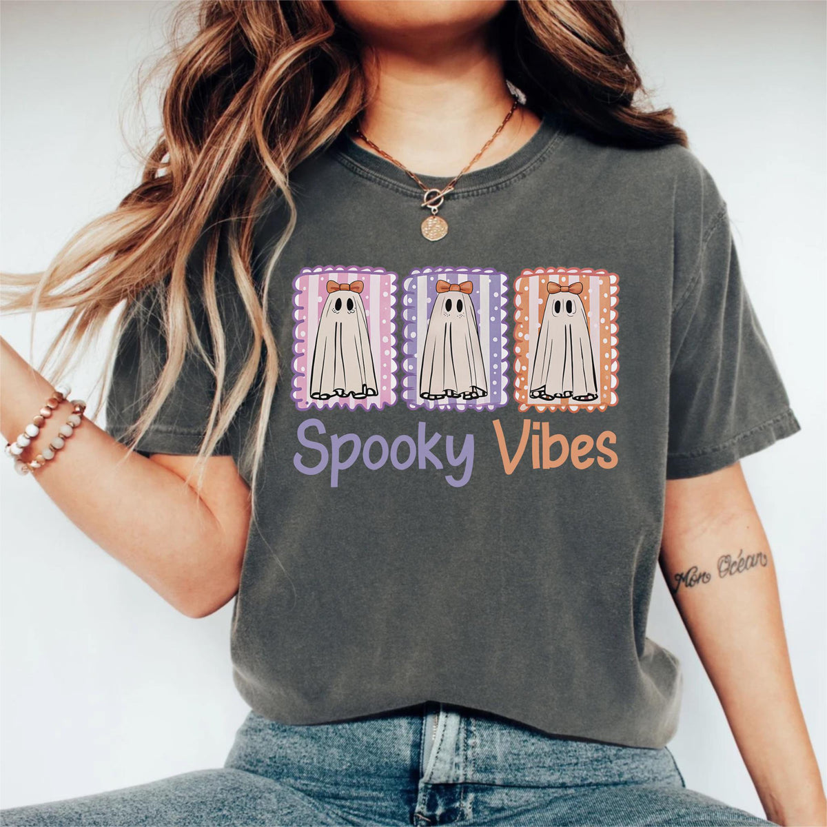 May include: Dark gray t-shirt featuring three cartoon ghosts in postage stamp frames. Each ghost has a bow and is set against a different color background. The text "Spooky Vibes" is below the ghosts in purple and orange.