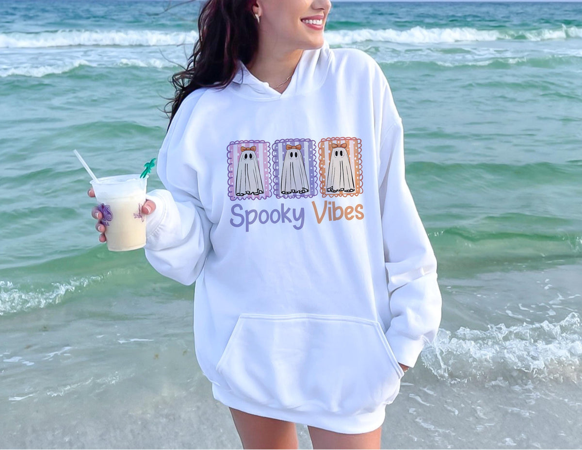 May include: White hooded sweatshirt with a front pocket and the words "Spooky Vibes" in purple and orange. The sweatshirt features a graphic of three ghost stamps in purple, orange, and lavender.