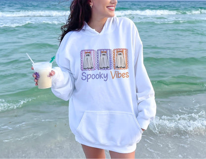 May include: White hooded sweatshirt with a front pocket and the words "Spooky Vibes" in purple and orange. The sweatshirt features a graphic of three ghost stamps in purple, orange, and lavender.
