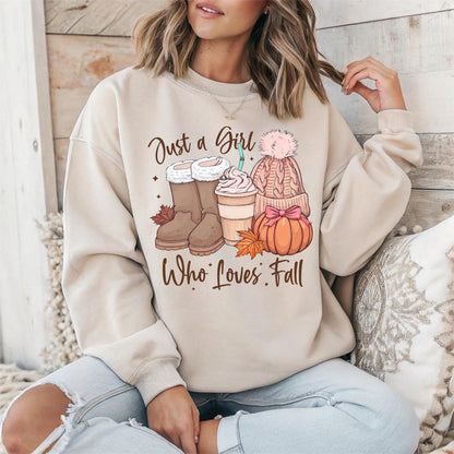 May include: Beige sweatshirt with a fall-themed graphic. The graphic includes brown boots, a coffee cup, a pink pom-pom hat, and a pumpkin. The text reads "Just a Girl Who Loves Fall."