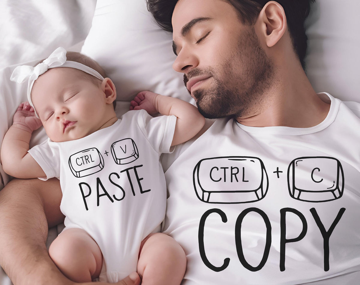 May include: A white onesie with the text "CTRL + V PASTE" and a white headband on a baby. A man wearing a white t-shirt with "CTRL + C COPY" sleeps next to the baby. The image is taken from above.
