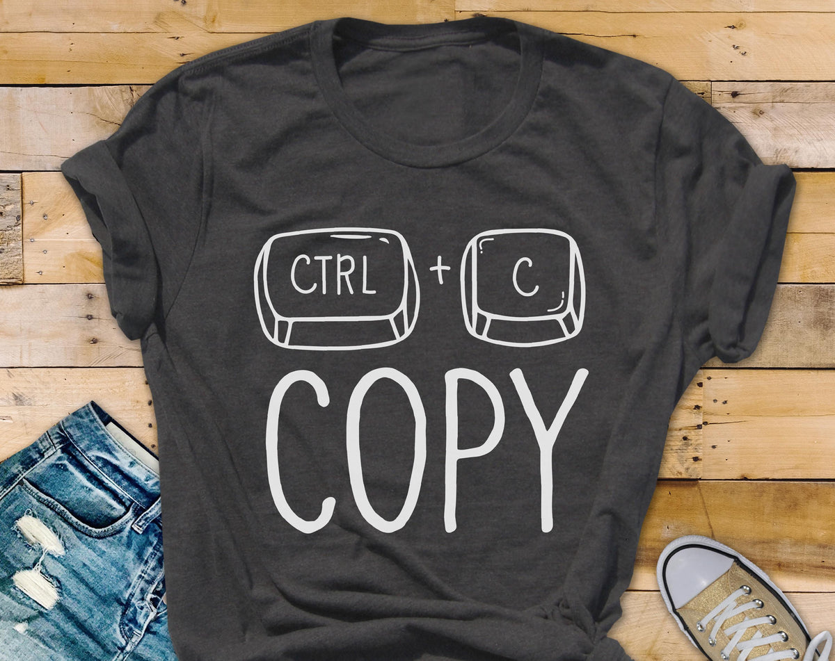 May include: Dark gray t-shirt with a white graphic of the CTRL and C keys, with the word "COPY" below. The shirt is folded at the sleeves and is paired with blue jeans and a canvas shoe.
