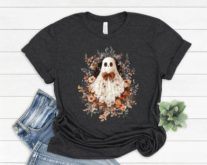 May include: Dark gray t-shirt featuring a whimsical ghost design. The ghost is adorned with a brown bow tie and surrounded by floral elements in shades of orange, brown, and cream. A perfect Halloween or fall-themed apparel.