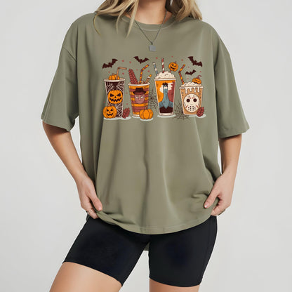 May include: Olive green t-shirt featuring a Halloween-themed graphic of four cartoon beverages with jack-o'-lantern faces, bats, and pumpkins. The drinks have striped straws and are set against a cobweb background. The shirt is a relaxed fit.