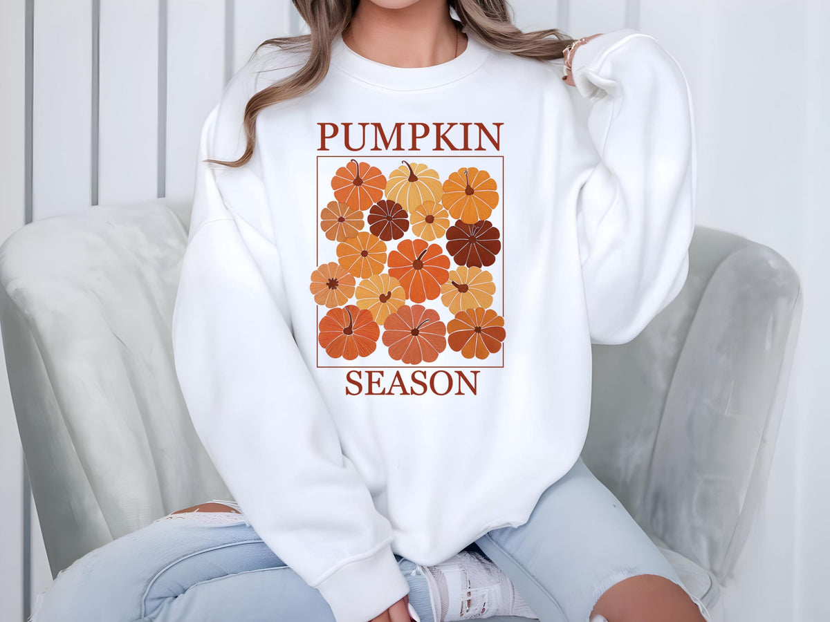 May include: White sweatshirt featuring a graphic of pumpkins in shades of orange and brown, framed by a rectangle. The words "PUMPKIN SEASON" are printed above and below the pumpkin graphic in a dark brown color.