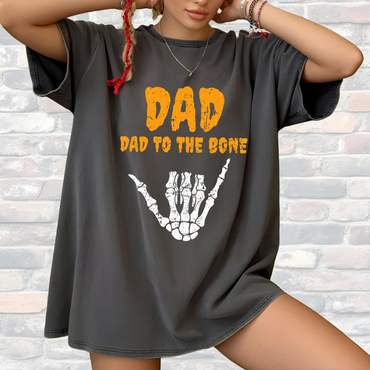 May include: Dark gray t-shirt with the text "DAD" in orange block letters above "DAD TO THE BONE." A white skeleton hand graphic is below the text. The shirt is a casual style.